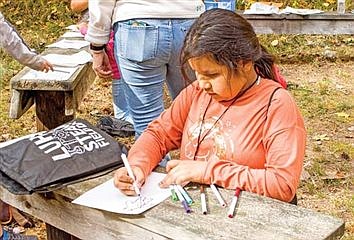 North Lakeland Elementary student Scarlet Wolfe draws a picture of a gingerbread man in colorful chocolate icing as part of an activity involving sharing traditions. (Photo by Jake Schexnaydre/Lakeland Times)
