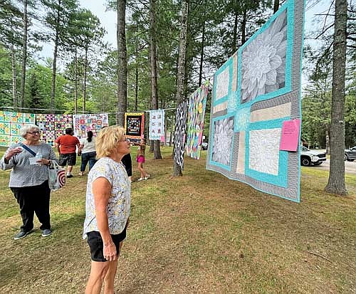 Lynn Cox takes a moment to appreciate the stitch work on one of the many quilts displayed during the 8th Annual Street Fair on Sunday, Aug. 6, in downtown Sayner. (Photo by Trevor Greene/Lakeland Times)