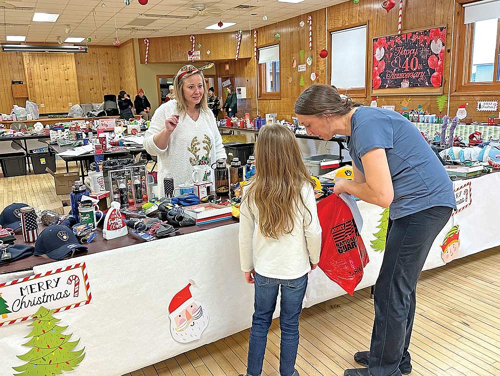 Jess Edwardson (in white sweater), president of the Sugar Camp School Community Organization (SCO), helps a student shop for Christmas gifts at the Santa’s Workshop event Friday, Dec. 16, 2023 at the Sugar Camp Town Hall. This year marked the 40th anniversary of Santa’s Workshop. For more on the event, see Page 2. (Photo by Heather Schaefer/River News)