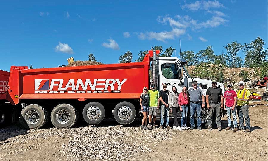 Members of Flannery Materials, from left, Mary Desrochers, Mike Desrochers, Dominic Schoen, Keara Schoen, Veronica Desrochers, Jamey Flannery, Matt Brazzow, Isaac Schoen and Jeremy Flannery show off one of the Flannery Materials dump trucks. (Photo by Mikey Rottier/Lakeland Times)