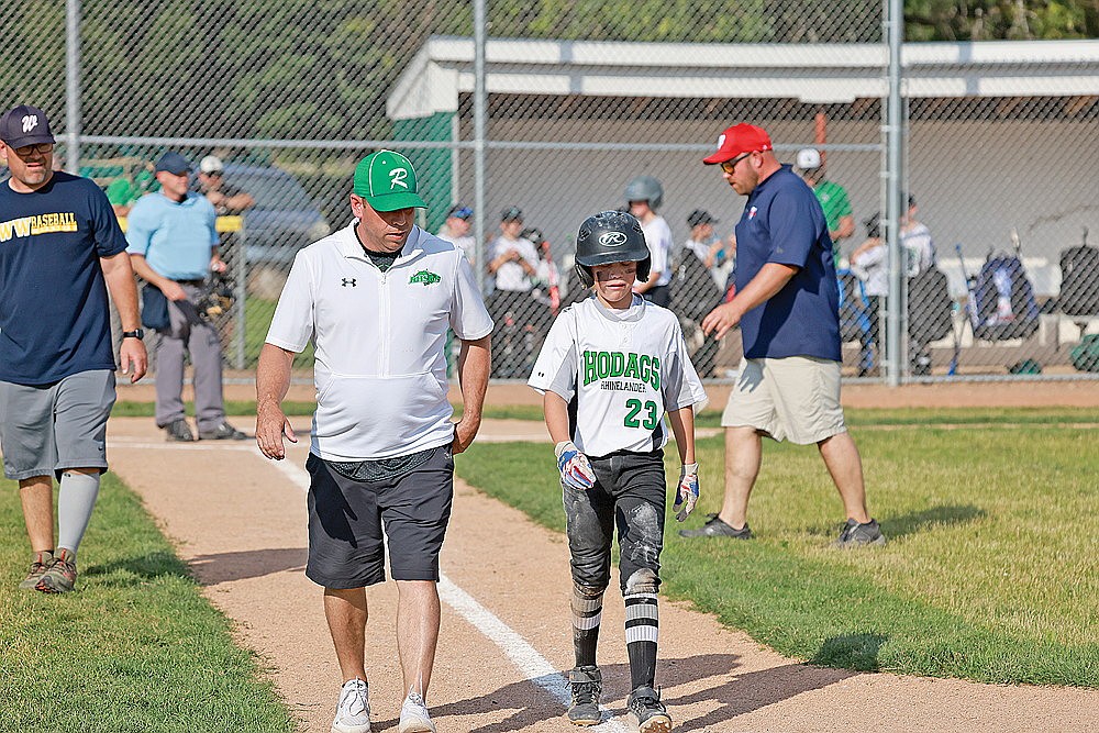 Rylan Pasanen walks to first with coach Brian Paulson after getting hit by a pitch during a game against Wausau American Tuesday, July 9. (Bob Mainhardt for the River News)