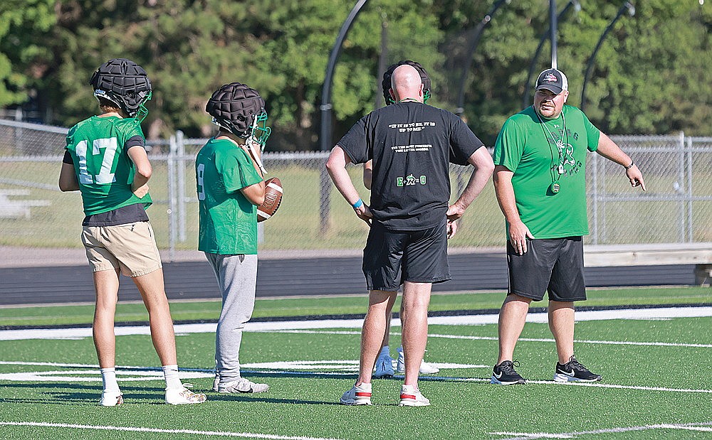 Rhinelander High School football coach Aaron Kraemer talks with quarterbacks Abe Gretzinger (17), Chandler Servent (9) and Truman Lamers — obstructed from view by assistant coach Luke Roberts — during practice at Mike Webster Stadium Tuesday, Aug. 6. Tuesday marked the first day high school football teams could practice in Wisconsin. (Bob Mainhardt for the River News)