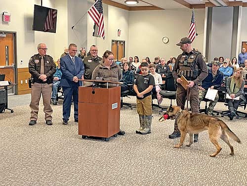 Gathered at the podium during the Jan. 28 Vilas County board meeting to honor Jackson Favorite are, from left, Pat Schmidt, chief deputy for the Vilas County Sheriff’s Office; Vilas County Sheriff Joe Fath; Gerard Ritter, a captain with the Vilas County Sheriff’s Office; Michelle Favorite, Jackson Favorite, Vilas County Sheriff’s Deputy Zach Stern and K-9 Officer Helo. (Photo by Brian Jopek/Lakeland Times)