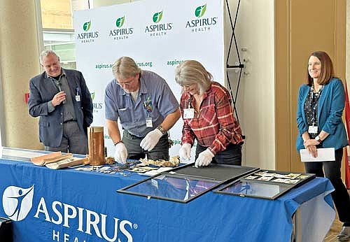 Aspirus North Region President Teri Theiler, far right, and Aspirus Community Engagement Coordinator Matt Thompson, far left, look on as Aspirus maintenance worker Jerry Hirman and environmental services associate Peggy Kaczmarek carefully remove items from a 1980s-era time capsule on Monday, Feb. 3, 2025. The canister, which contained medallions, coins, a scroll and several rosaries, was found behind the cornerstone of the former St. Mary’s Hospital building on Kabel Avenue in Rhinelander. (Photo by Heather Schaefer/River News)