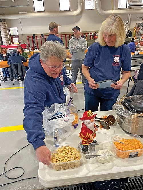 Debbie Jelinek, left, and Nancy Voelker prepare the Nokomis fire department’s display as the Seventh Annual Firehouse Chili Feed Challenge got underway in Minocqua on Feb. 22. (Photo by Brian Jopek/Lakeland Times)