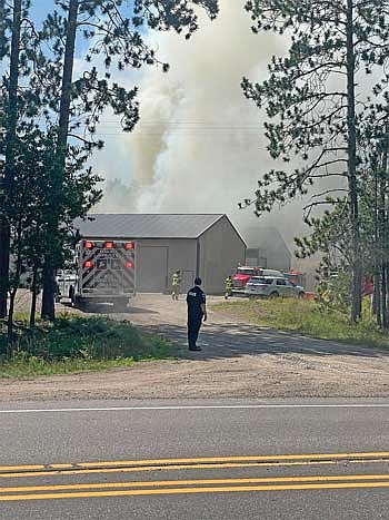 With smoke from a fire in storage units billowing in the background, Minocqua police officer Ben Burrows stands in the entrance to LNK Rentals on State Highway 47 on Saturday, July 26. (Photo by Brian Jopek/Lakeland Times)
