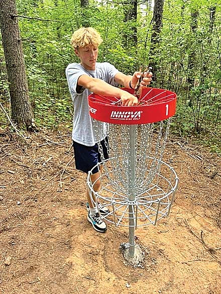 Cody Vojta completes installation of the first basket at St. Germain’s new community disc-golf course on Thursday, Aug. 14. (Photo by Fred Williston/Lakeland Times)
