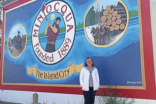 Joan Christgau in front of the Paul Bunyan mural in downtown Minocqua. Christgau said she recieves a lot of feedback about this particular mural due to it’s bold and striking colors. (Photo by Michael Strasburg/Lakeland Times)
