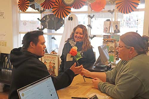 LUHS student Cameron Jack offers a couple roses to Northern Nest owner Trisha Tapaninen as a random act of kindness while florist Jana Acheson looks on. (Photo by Michael Strasburg/Lakeland Times)