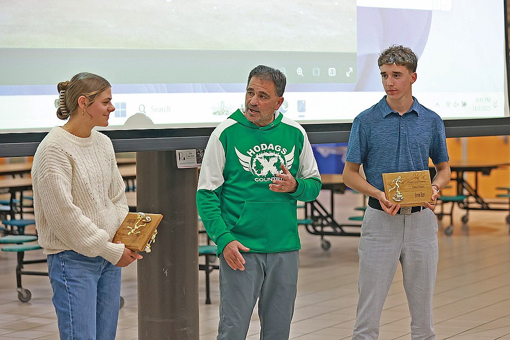 Macy Myers, left, and Avrom Barr, right, listen as coach M.J. Laggis speaks during the Rhinelander High School cross country team banquet in the RHS commons Sunday, Nov. 2. Myers and Barr earned the team’s fastest harrier awards for the 2025 season. (Bob Mainhardt for the River News)