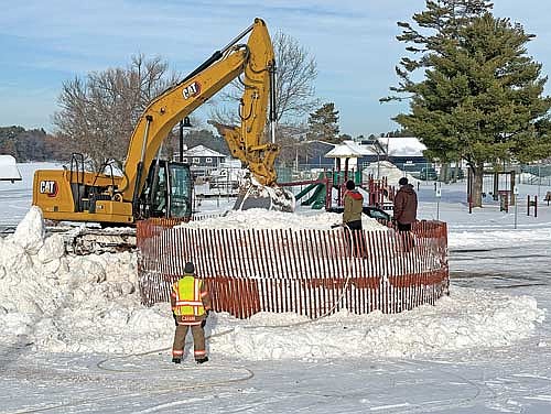 Minocqua fire chief Rich Carani watches as employees with Schrom’s Excavating spray down snow to freeze while building the giant snowman known as Snowmy Kromer at Torpy Park on Tuesday, Dec. 16, in Minocqua. (Photo by Trevor Greene/Lakeland Times)