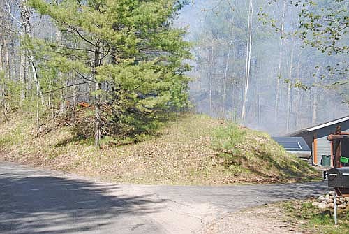 The early stages of a fire on Kobart Road in Minocqua before firefighters arrived; the area behind the garage had already burned and the wind was spreading the fire, moving away from the residence. It ultimately did move toward a neighbor’s house to the north and east and firefighters were able to stop it. (Photo by Brian Jopek/Lakeland Times)