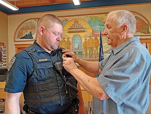 George Rezny, right, pins a gleaming golden police sergeant badge on his son, Ryan, at the promotion celebration May 27 at City Hall. (Photo by Ardith Carlton/River News)