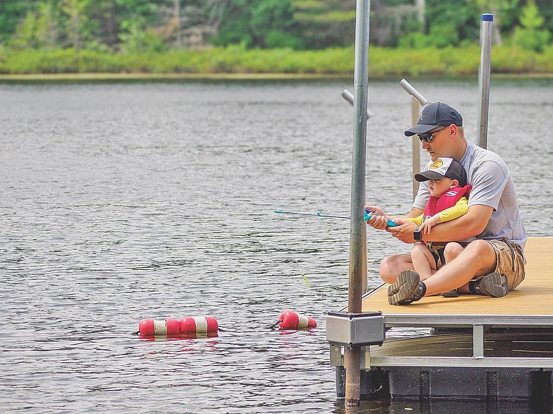 Josh Teske teaches his son Fischer, 1 year old, how to fish during the North Lakeland Discovery Center’s Summer Family Play Day on Thursday, July 2, in Manitowish Waters. (Photo by Sharyn Umaña/Lakeland Times)