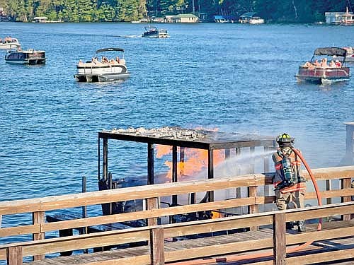 With lakegoers watching, a Minocqua firefighter pours water on a boat fire at the public pier next to the U.S. Highway 51 bridge over Lake Minocqua on Sunday, Aug. 2. (Photo by Sharyn Umaña/Lakeland Times)